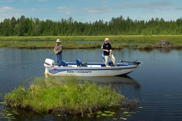 Two men fishing on a boat in the lake.